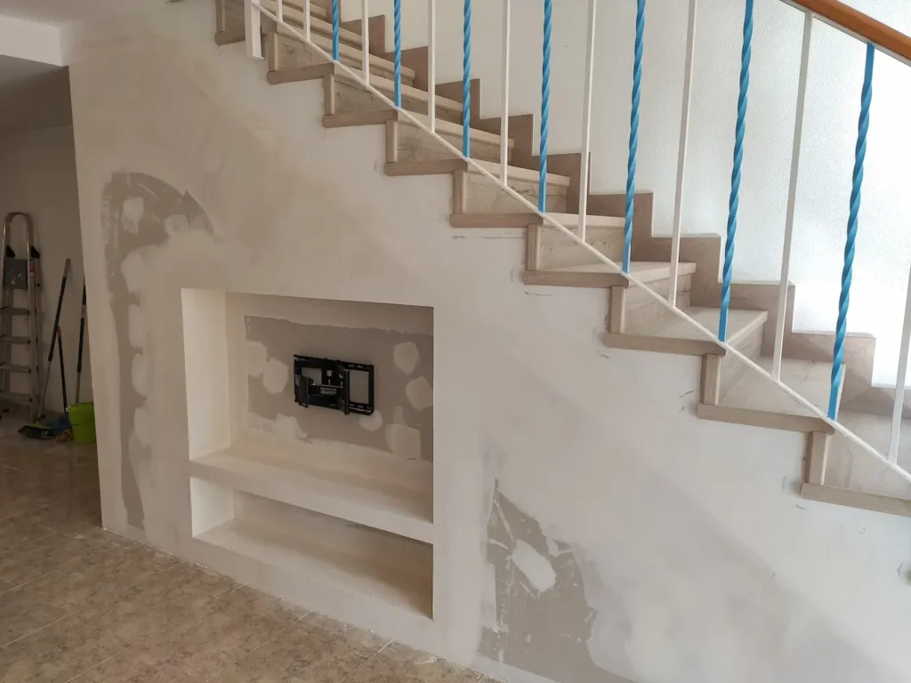En la imagen vemos un mueble de pladur para poner una televisión y una balda aprovechando el hueco de escalera